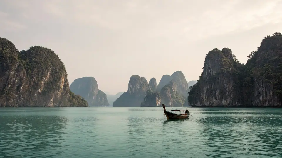 Limestone islands and a longtail boat on calm water in Thailand